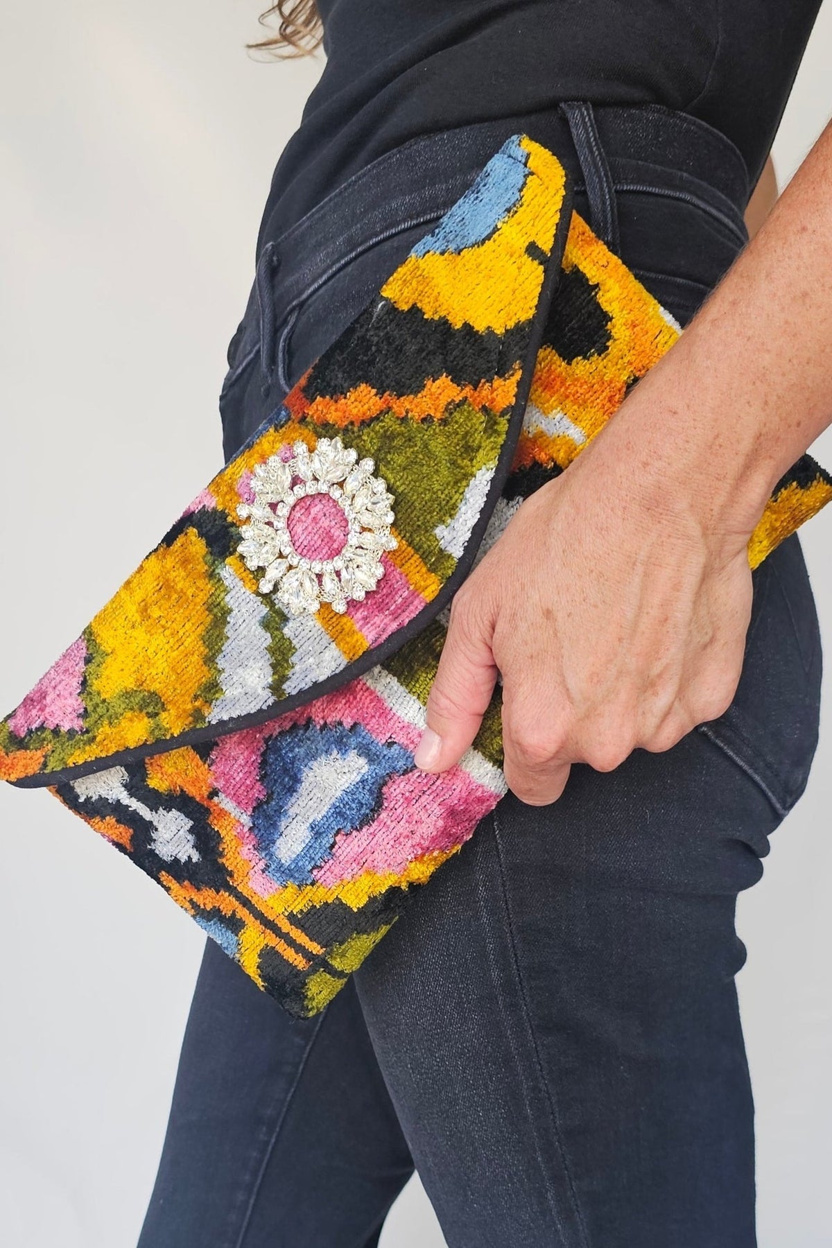 Person holding a colorful embroidered clutch bag against a plain background