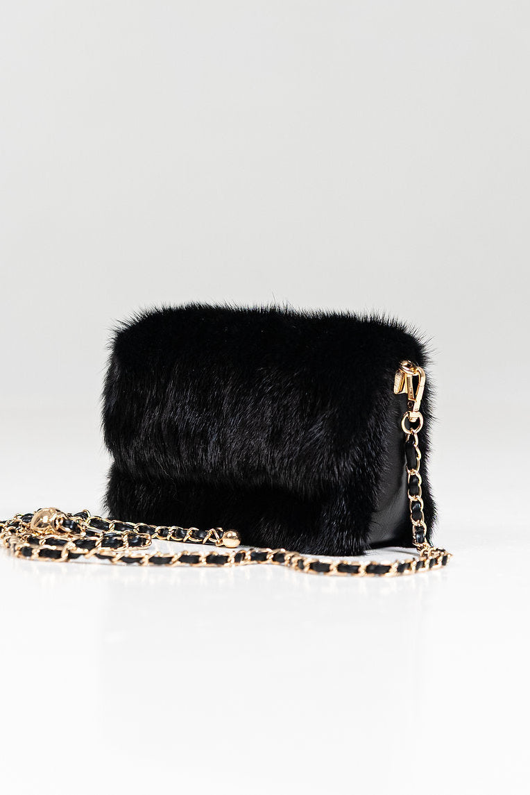 Black fur handbag with gold chain strap on a light gray background
