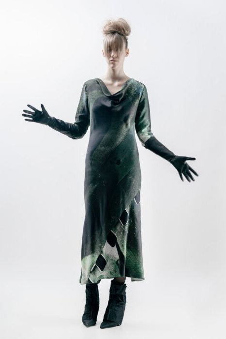 Person wearing a long, dark green dress with geometric patterns on a white background